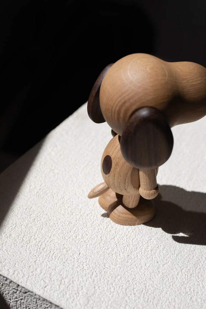 A Boyhood Snoopy, Large toy leans over the edge of a white table, casting a long shadow in the bright sunlight. Its paw extends outward as if reaching for something below.