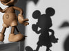 A wooden figure named Mickey Mouse, Oak is partially visible on the left, casting a shadow on a gray wall. The shadow reveals Mickey Mouse’s iconic round ears and gloves, capturing the adventurous spirit of this global icon.