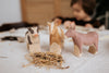 A donkey, cow, and horse, all handcrafted from linden wood with child-safe paint, stand on a table covered in straw-like material. A blurred child adds to the cozy atmosphere. The donkey is from the Handmade Wooden Donkey collection.
