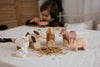 A child plays at a table with handcrafted wooden toys, including a Handmade Wooden Pig painted with child-safe colors. Created with care in Serbia, the scene exudes warmth and coziness.