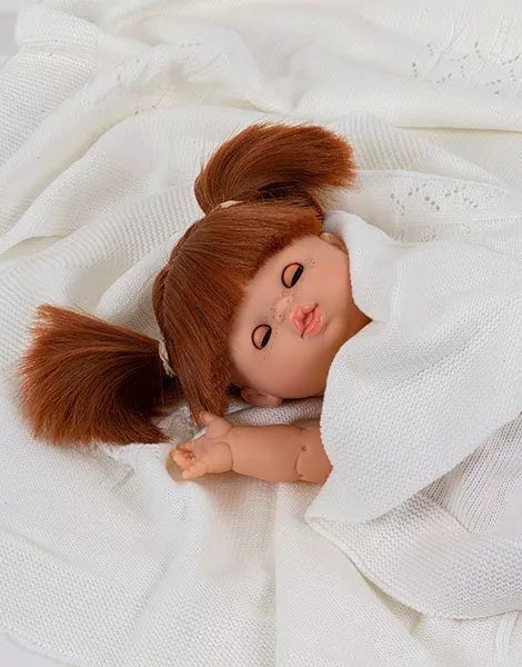 The Minikane Baby Doll With Sleeping Eyes (13") - Raphaelle with brown hair in pigtails, wrapped in a soft white blanket, rests peacefully on a white fabric background, exuding a gentle natural vanilla scent.