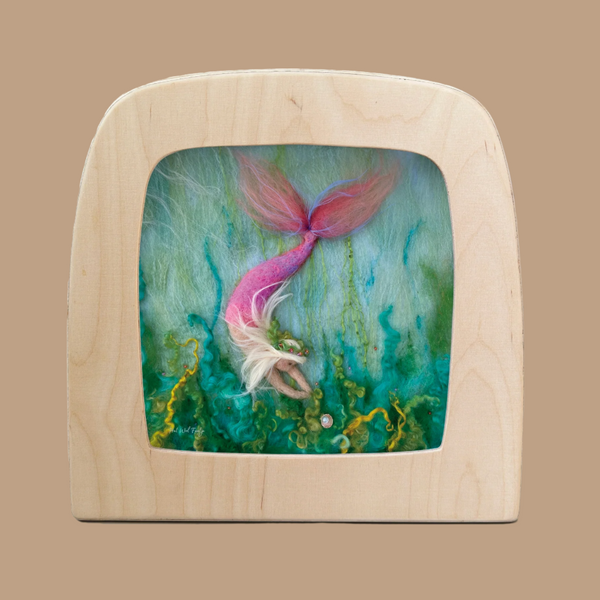 The "Silhouette Only - Mermaid for Toverlux Lamp" is a felt art piece featuring a mermaid with pink tail and flowing hair diving underwater, amidst green and blue ocean hues contrasted by yellow seaweed, beautifully framed in light wood to enhance any home atmosphere.