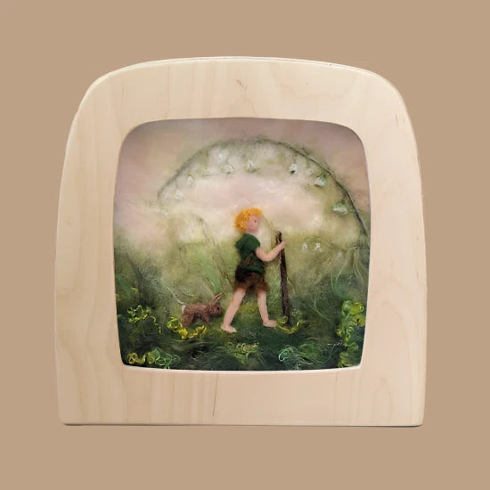 A felt artwork titled "Silhouette Only - Little Explorer" captures a person with orange hair and a dog walking through a misty green landscape. Surrounded by swirling plants, they hold a staff, creating magical silhouettes in the haze. The piece is elegantly showcased in a light magic window frame and ships in approximately one week.