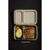 A Haps Nordic - Stainless Steel Lunch - Two Compartments rests on a black background. The smaller compartment contains assorted cherry tomatoes and a halved avocado, while the larger compartment holds a slice of seeded multigrain bread. The top of the box is open.