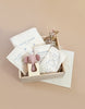The Newborn Gift Set is a wooden box of newborn accessories, including a hooded swaddle, pilot hat, bib, and mittens made from organic cotton in elegant cream packaging. A charming small wooden toy completes this perfect baby gift against a neutral beige backdrop.