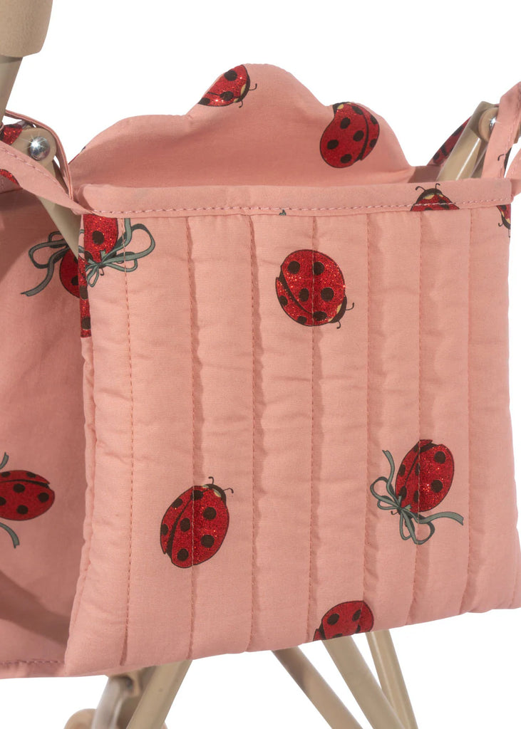 The Konges Sloejd Doll Stroller features a vibrant ladybug pattern on pink quilted fabric, elegantly draped over the frame. The focus is on its lively design with removable fabric, offering ease and versatility.