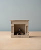 A small, beige miniature fireplace with tiny logs sits on a light surface beside the Maileg Moms Afternoon Tea Set, against a plain, light blue background. Choking hazard—keep out of reach of young children.