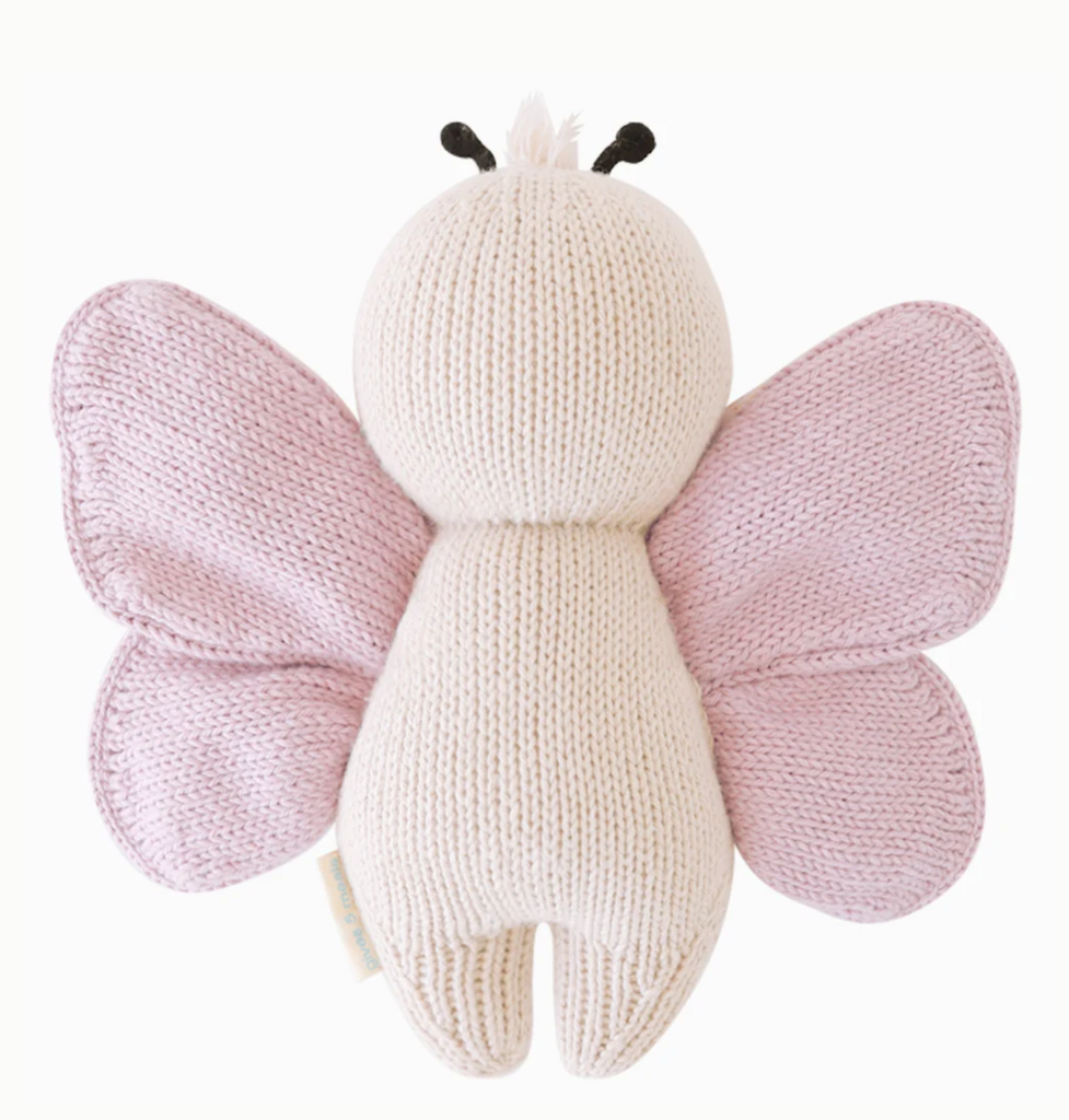 A Cuddle + Kind Baby Butterfly made from soft Peruvian cotton yarn features a light beige body and delicate light pink wings. This collectible piece has small black antennae on its round head and stands upright with no facial features visible, making it a charming addition to any hand-knit baby animals collection.