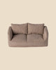 A small fabric sofa with a brown and gray checkered pattern sits beside a Maileg Living Room Set Soft Chair, featuring two cushions and armrests against a plain beige background.