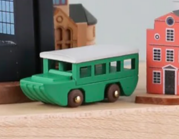 A Replacement Boat for a Boston Music Box sits on a wooden surface, encircled by miniature wooden buildings, creating an imaginative urban scene.
