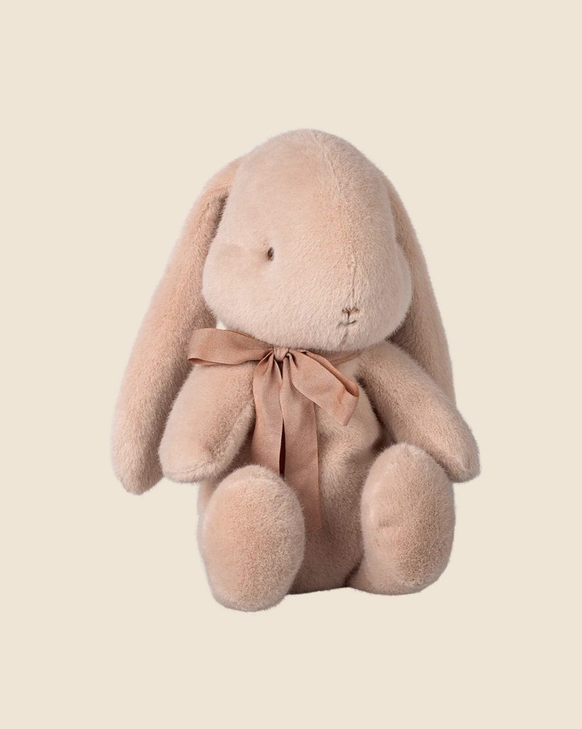 A medium light powder Maileg Plush Bunny with long ears and a brown ribbon sits against a cream background, available for pre-order and shipping in February.