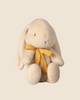 A medium cream Maileg plush bunny, made from recycled polyester with floppy ears and a yellow ribbon, sits against a plain beige background. Available for pre-order now and ships in February.