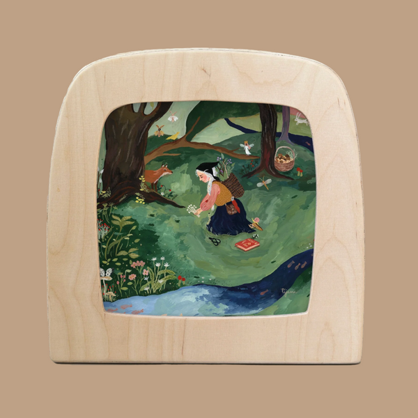 The Silhouette Only - Foraging for Toverlux Lamp features a wooden-framed illustration of a person gathering in a lush forest, surrounded by trees, flowers, and birds with a basket. This scene beautifully integrates Magic Silhouettes into its light brown background.