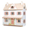 Image of a white, two-story dollhouse with pink shutters and doors, a beige roof, and a wrap-around porch. The Humming Bird Dollhouse features detailed windows and a decorative front door, evoking a charming, classic style. The overall aesthetic is whimsical and inviting.