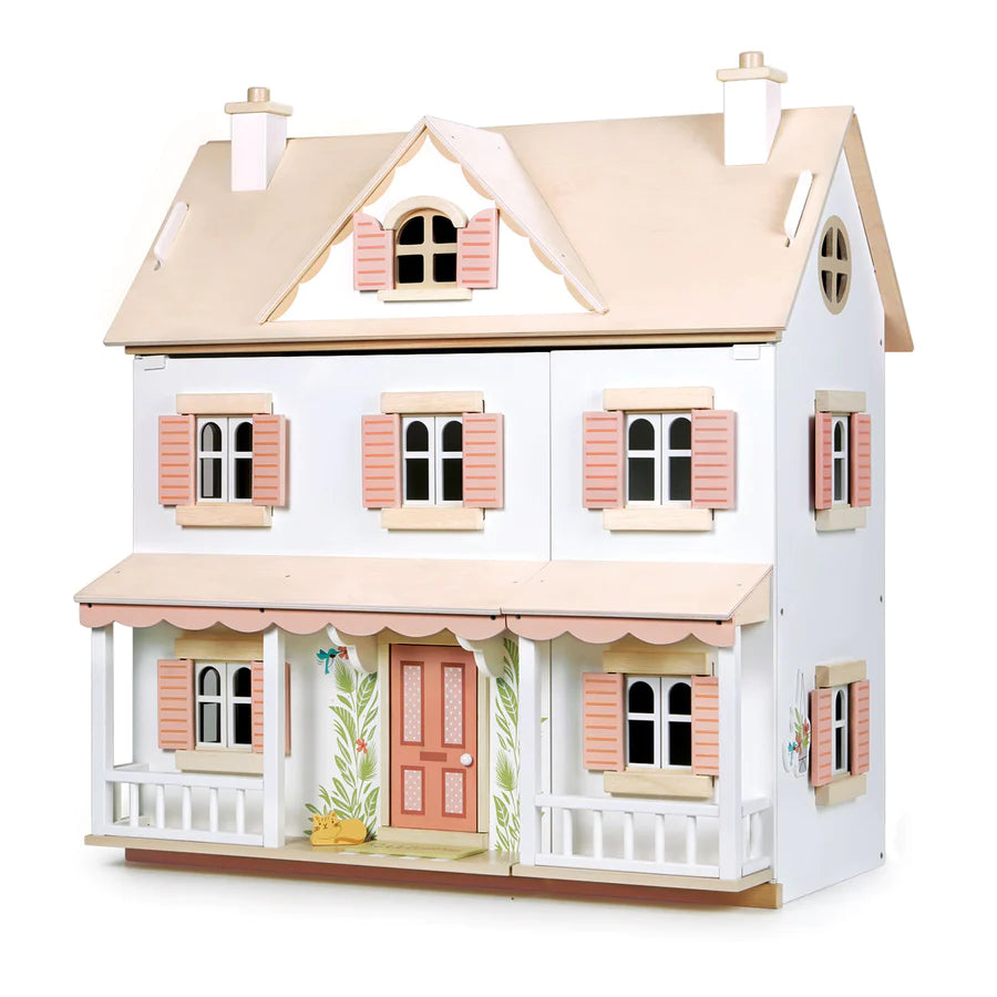 Image of a white, two-story dollhouse with pink shutters and doors, a beige roof, and a wrap-around porch. The Humming Bird Dollhouse features detailed windows and a decorative front door, evoking a charming, classic style. The overall aesthetic is whimsical and inviting.