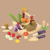 The Wild Wood Foraging Trug features a wooden toy set with fruits, vegetables, and gardening tools on a brown background. It includes cherries, grapes, mushrooms, foraged plants, a handled basket, and a small shovel to inspire kids in imaginative play.