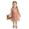 Barefoot, a young girl in a peach dress beams as she holds the Wild Wood Foraging Trug, filled with colorful toy fruits and vegetables. A whimsical recipe leaflet inside hints at fun culinary adventures against a pristine white backdrop.