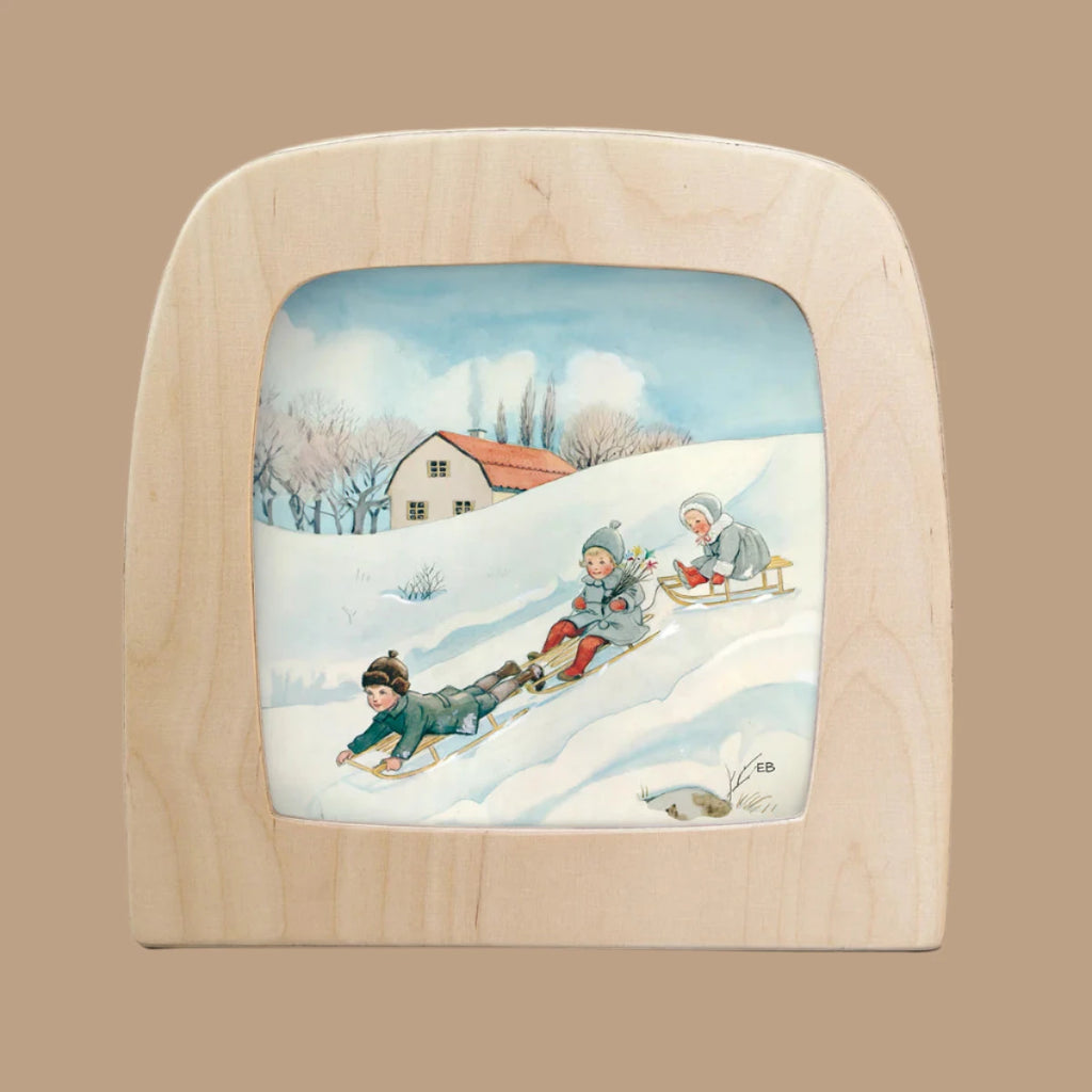 The "Silhouette Only - Around The Year (February) for Toverlux Lamp" depicts a winter scene with three children sledding downhill, bundled in warm attire, watched by a cozy house with a red roof amidst snowy trees, evoking enchanting Magic Silhouettes.