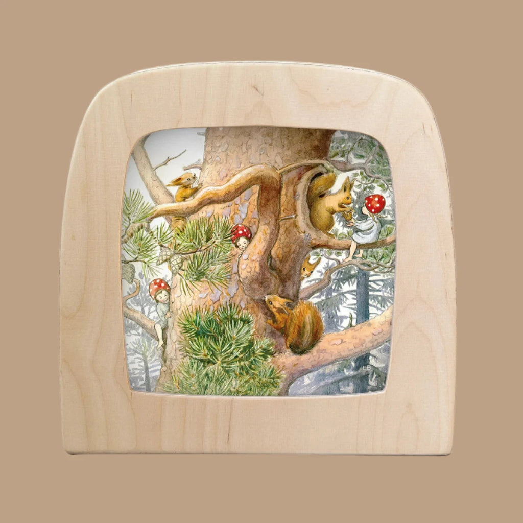 The Children of the Forest silhouette features a magical scene with two squirrels and a bird on a tree with glowing mushrooms. Set within a wooden frame resembling a window, this enchanting design adds mystery against snow-covered forest trees, perfect for your Toverlux Lamp.