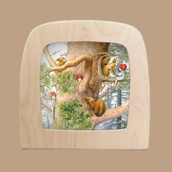 The Children of the Forest silhouette features a magical scene with two squirrels and a bird on a tree with glowing mushrooms. Set within a wooden frame resembling a window, this enchanting design adds mystery against snow-covered forest trees, perfect for your Toverlux Lamp.
