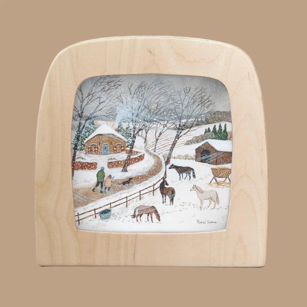 A wooden frame showcases "Silhouette Only - Cold Snap for Toverlux Lamp," an illustration of a snowy rural scene with someone feeding horses by a barn, bare trees, a winding path, and snow-covered hills. The image exudes rustic, wintery charm reminiscent of Magic Silhouettes dancing in the crisp air.