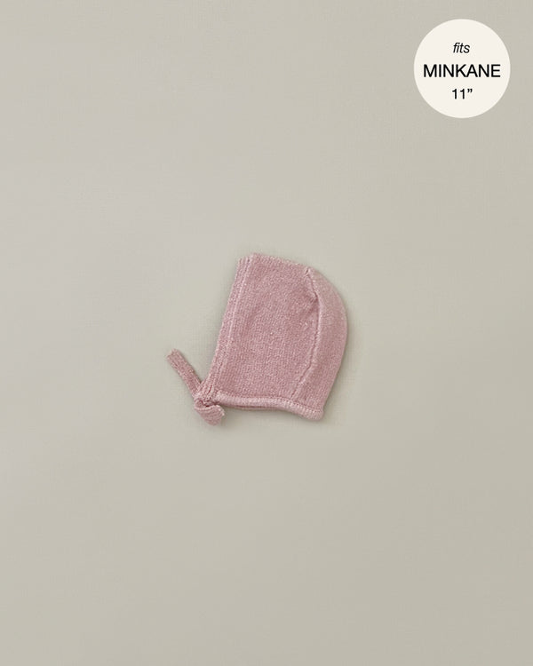 A small pink knitted bonnet, perfect for Minikane Babies, is displayed on a plain light gray background. The text "fits MINKANE 11"" is shown in the upper right corner inside a white circle. The product name is Minikane Doll Clothing | Élie Tea Pink Knit Bonnet.