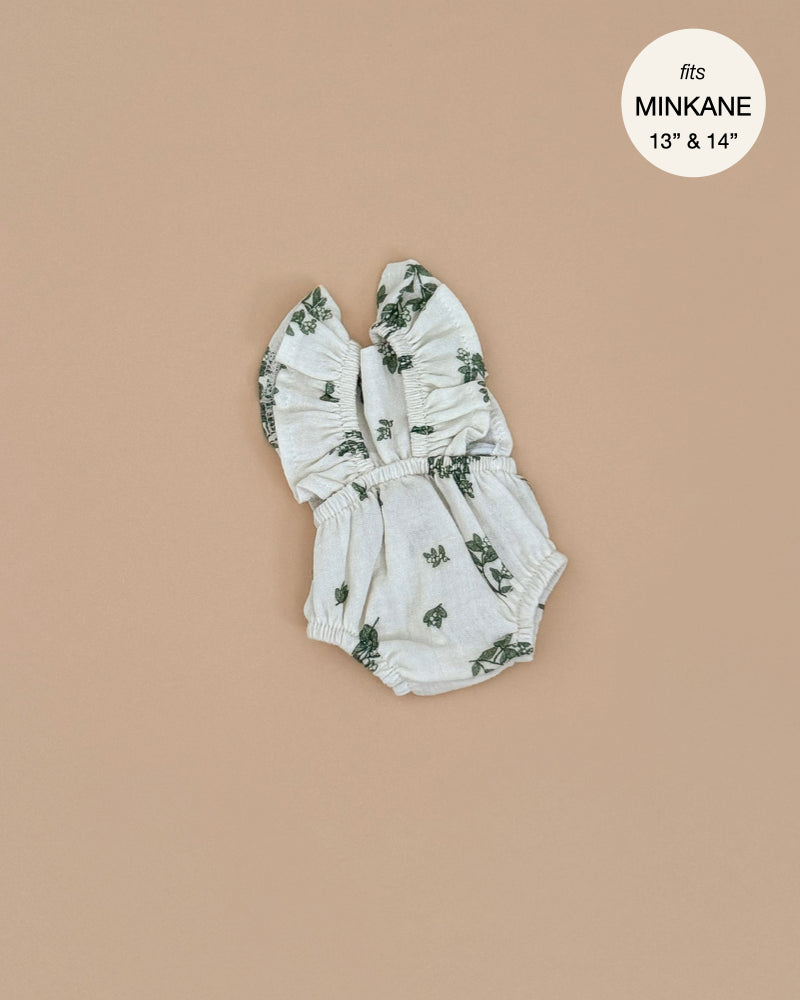 The Minikane Doll Clothing Lou Retro Romper, a sleeveless romper with ruffled straps and a light gray floral pattern, is elegantly displayed on a beige background. Designed in France to fit 13" and 14" dolls, the circular tag reads "fits Minikane 13” & 14”.