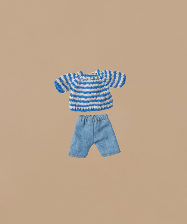 The Maileg Knitted Sweater, featuring blue and white stripes, is matched with denim shorts on a plain beige backdrop.