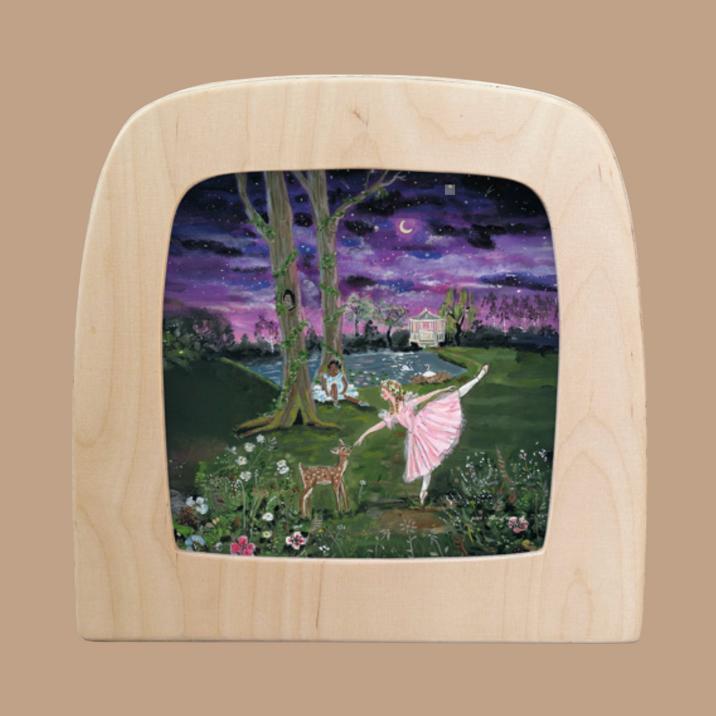 The "Moonlight Ballerina for Toverlux Lamp" features a framed silhouette of a ballerina in pink, dancing by a deer and rabbit near a pond. A crescent moon and stars cast an enchanting glow, with a house framed by trees and flowers in the background.