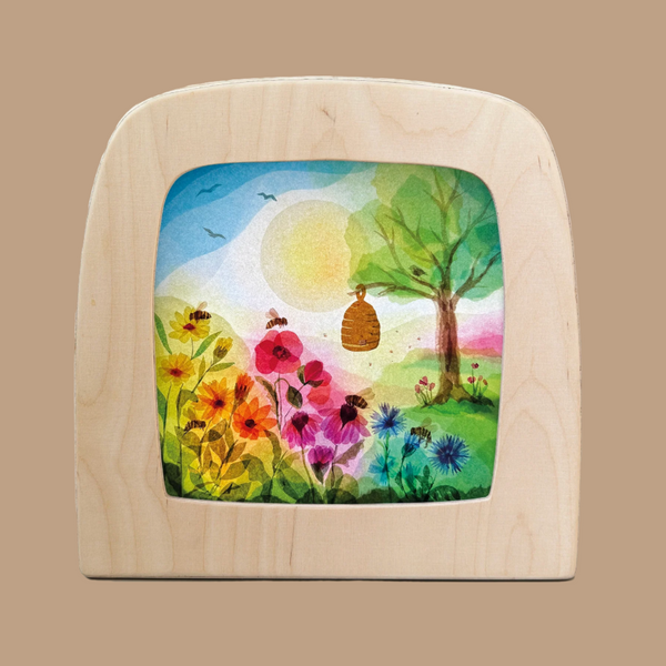 A wooden-framed, colorful drawing by Toverlux showcases a sunny scene with a tree, flowers, birds, and a beehive. The sun radiates brightly like Magic Silhouettes in "Silhouette Only - Honeybees for Toverlux Lamp," casting a warm glow over the cheerful landscape.