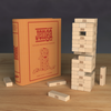 The Jenga Vintage Bookshelf Edition, styled like a book, stands upright by a partially played tower and loose wooden blocks—ideal for family game night on a wooden table.