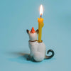 The Siamese Cat Cake Topper, a whimsical ceramic figurine with a red party hat and lit yellow candle, set against a light blue background, adds festive charm to any cat-themed party.