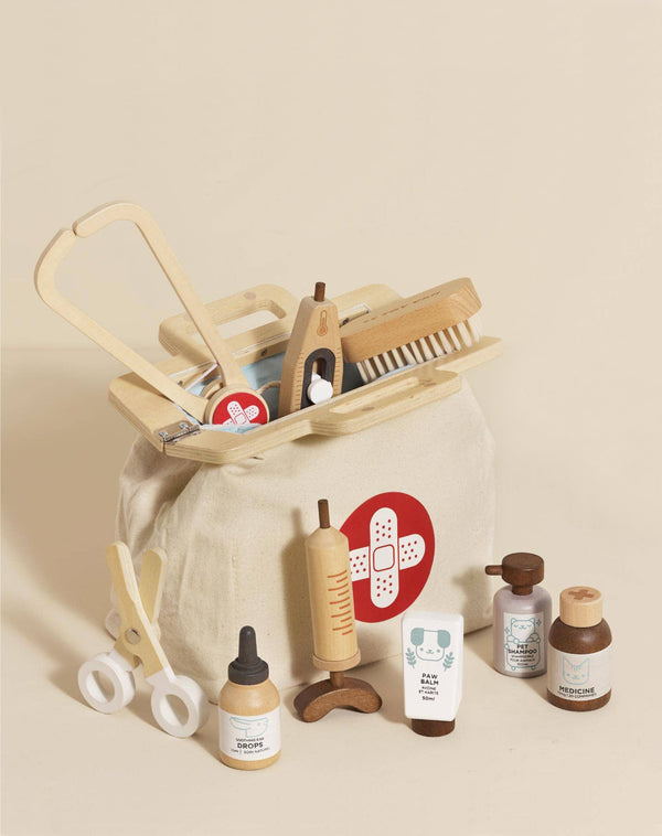 The Pretend Play Animal Vet Set features a beige fabric medical bag with a red and white cross, filled with wooden toy medical tools for career-based role play, ideal for aspiring vets. Displayed on a neutral background.