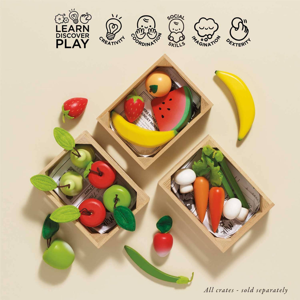 The Orchard Fruits Wooden Market Crate features toy strawberries, a watermelon slice, bananas, wooden apples and pears, carrots, mushrooms, a green pea, and a chili pepper in three wooden crates on a beige background. Icons and text highlight its learning benefits.