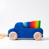 The Grimm's Pull Along Truck features natural wooden wheels, a non-toxic design, and an orange string for easy play. It carries rainbow-colored blocks stacked from red to green against a plain white background.