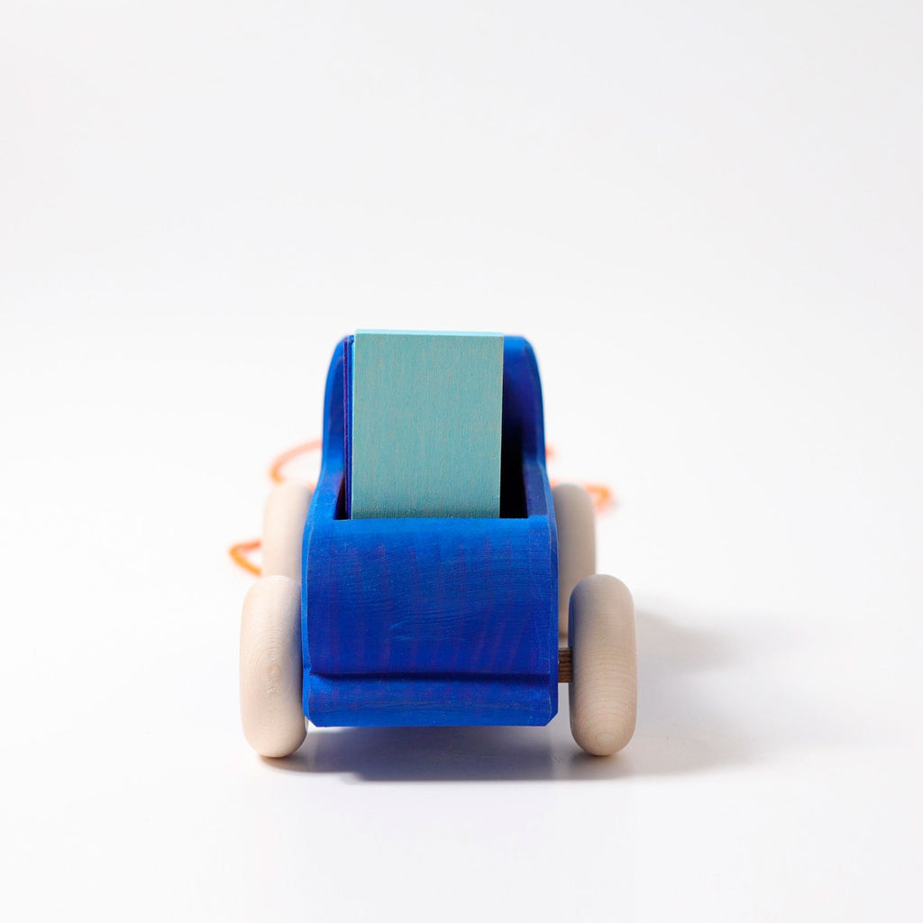 Grimm's Pull Along Truck features a vibrant, non-toxic blue wooden body with light wood wheels set against a white backdrop. An orange string gracefully drapes from the front, perfect for pulling.
