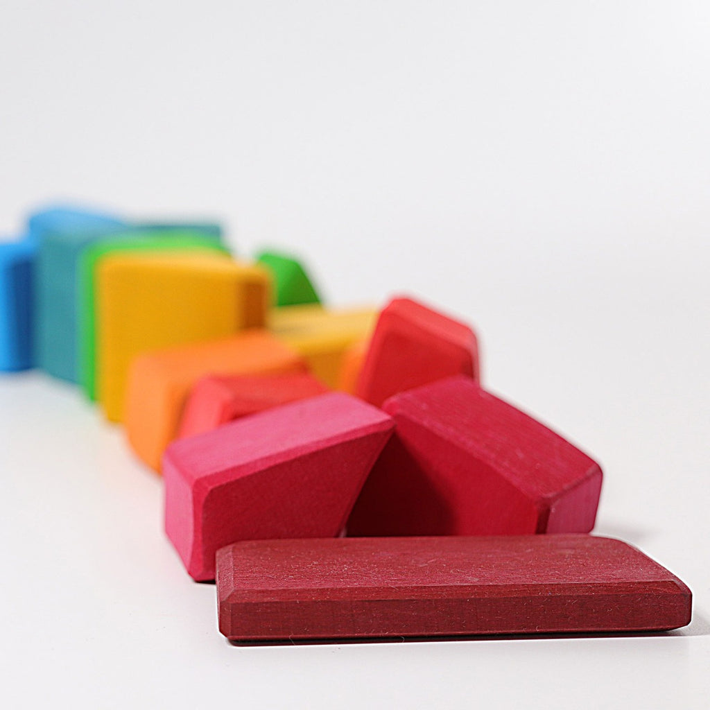 Grimm's Colored Waldorf Blocks, crafted for open-ended play and non-toxic fun, are arranged like dominos on a white surface with colors such as red, orange, yellow, green, and blue. The red blocks take center stage.