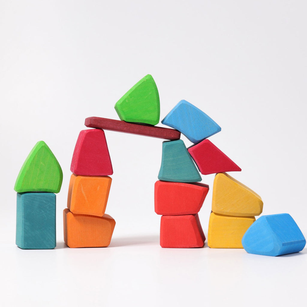 Grimm's Colored Waldorf Blocks, in vibrant blue, green, red, yellow, and orange hues and various shapes, form a non-toxic wooden arch against a white background—ideal for open-ended play.