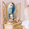 A child explores the Wooden Beauty Kit at a wicker vanity with a butterfly design. Non-toxic toy makeup is scattered around for safe fun, while a figure watches over in the pink-walled room—a classic timeless toy experience.