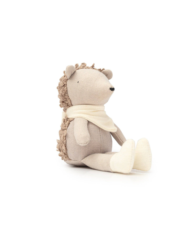 Poppet The Baby Hedgehog is a pocket-sized, textured beige and plain fabric toy. Sitting upright with a white scarf, its fabric mimics spikes on its back and smooth body and snout. It rests against a plain white background, ready to become your charming garden companion.