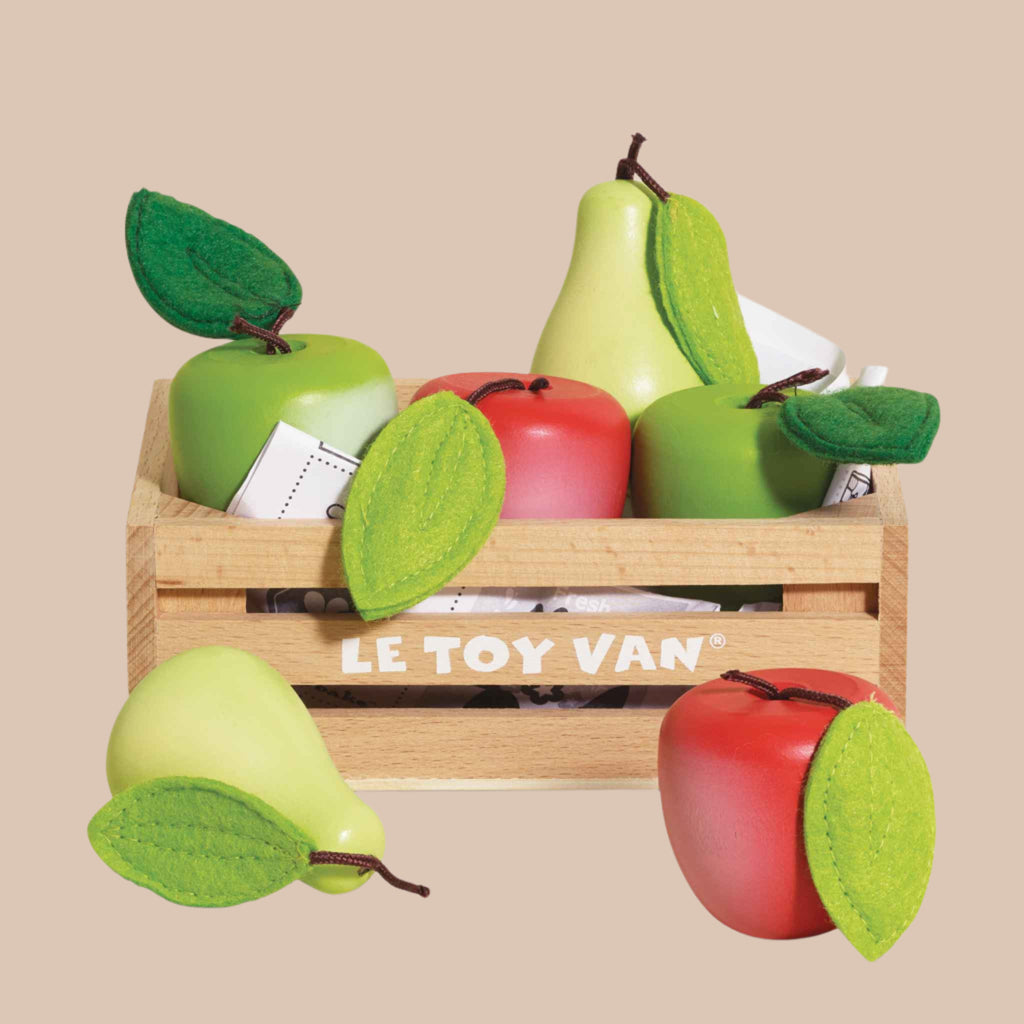 The "Orchard Fruits Wooden Market Crate" is a wooden crate featuring early-learning toy wooden apples and pears with felt leaves, branded by Le Toy Van. Perfect for role play, it's set against a solid beige background.