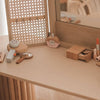 The Wooden Beauty Kit is showcased on a table, including wooden toys like a mirror, comb, powder compact, lipstick, and eye shadow. Non-toxic paint ensures safe play. A woven screen and large mirror in the background enhance the cozy vanity setup.