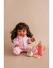 The My Tiny Birthday Set by Tiny Harlow features a doll with long brown hair seated on a beige surface, dressed in a pink onesie. In front of her are a pink baby bottle and a mini container styled like a birthday cake jar, evoking realistic play. The backdrop is plain light brown.