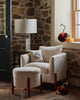A cozy interior featuring a plush white armchair with a Bat Wing Surprise Pillow resting next to a window with autumn pumpkins on the sill, all against an old stone wall.