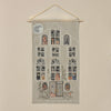 The Haunted House Advent Calendar is an embroidered fabric art piece designed as a multi-story haunted house. It features various Halloween characters, such as skeletons and pumpkins, visible through the windows. The house boasts intricate Halloween-themed decorations and a full moon glowing in the top left corner.