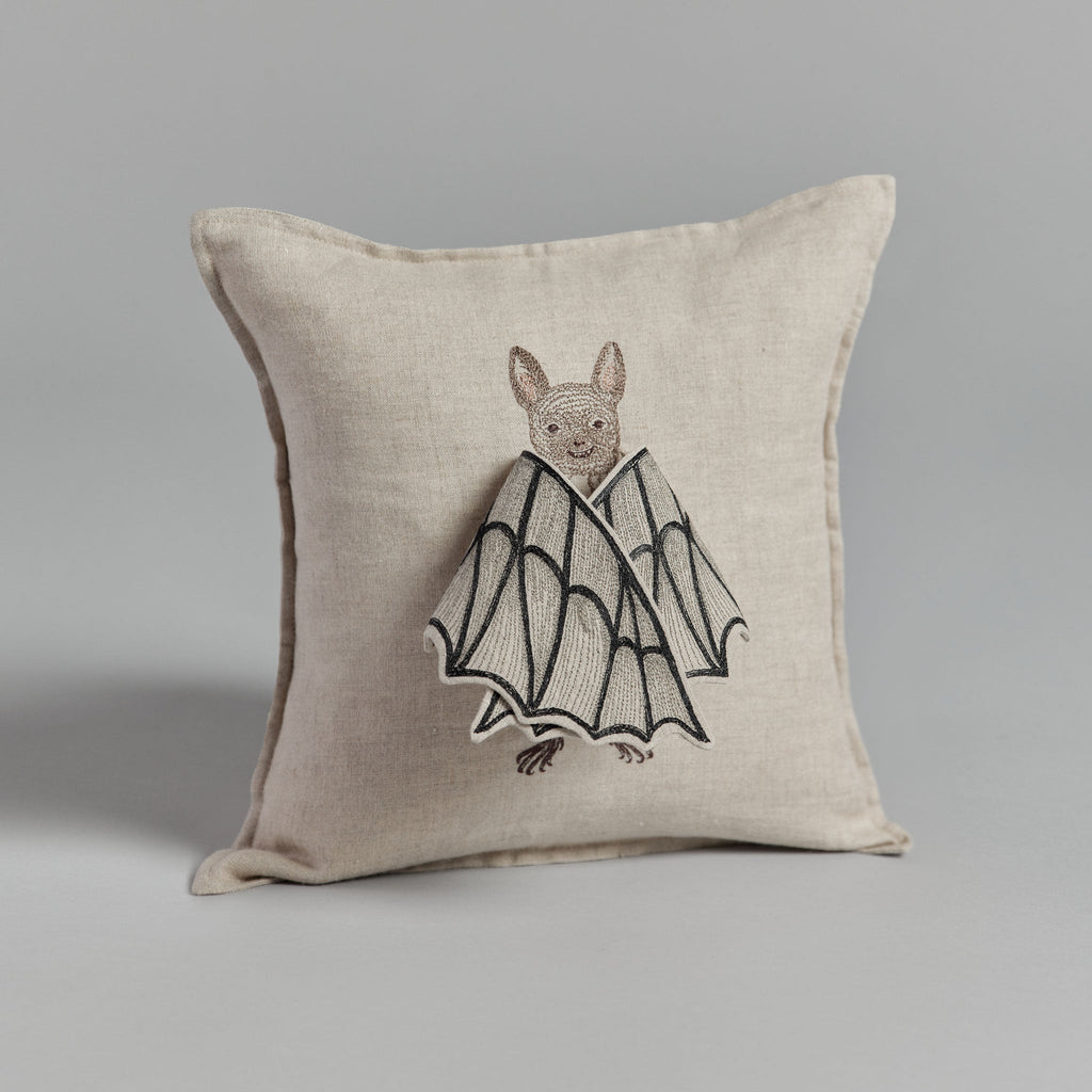 Decorative pillow with an embroidered design of a Bat Wing Surprise Pillow on a neutral linen background, photographed against a gray backdrop.