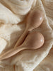 The Handmade Wooden Maracas, ideal for babies and toddlers to encourage motor skills, rest gently on a soft, cream-colored textured fabric.