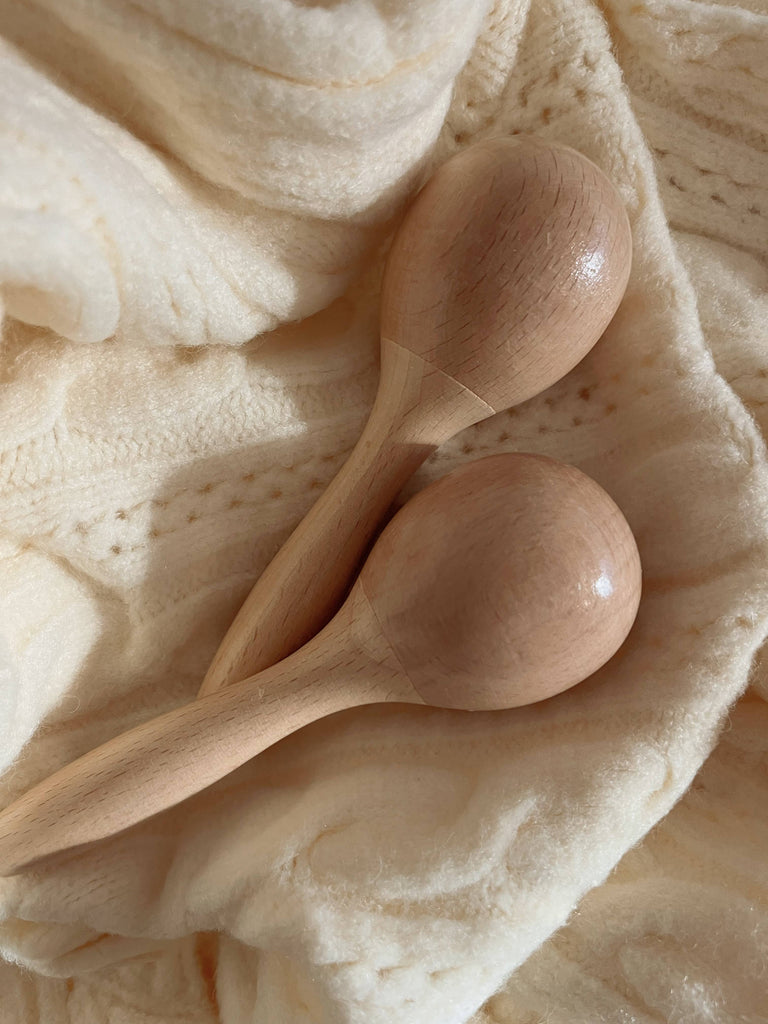 The Handmade Wooden Maracas, ideal for babies and toddlers to encourage motor skills, rest gently on a soft, cream-colored textured fabric.