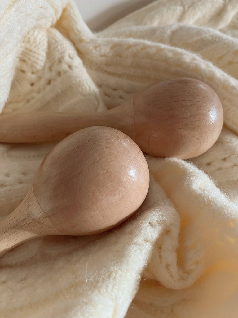 Handmade Wooden Maracas rest on a cream-knit blanket, their light wood paired with the soft texture to create a warm, inviting setting—ideal for nurturing motor skills during baby and toddler playtime.