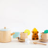 The Wooden Tea Set is ideal for a cozy play space, featuring a teapot, lemon-adorned cups, sugar cubes, a bear-shaped honey jar, a wooden spoon, and milk carton.